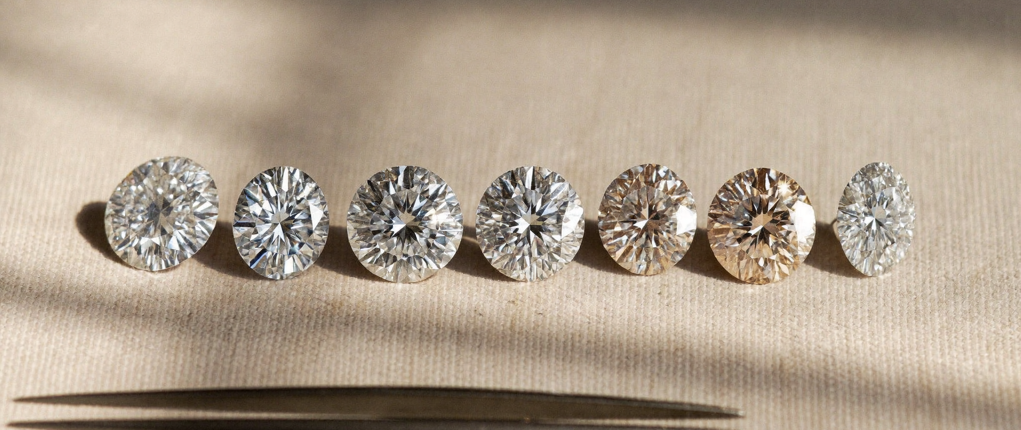 Row of lab-grown diamonds along the diamond color chart, from icy colorless to warm champagne, on linen in natural light