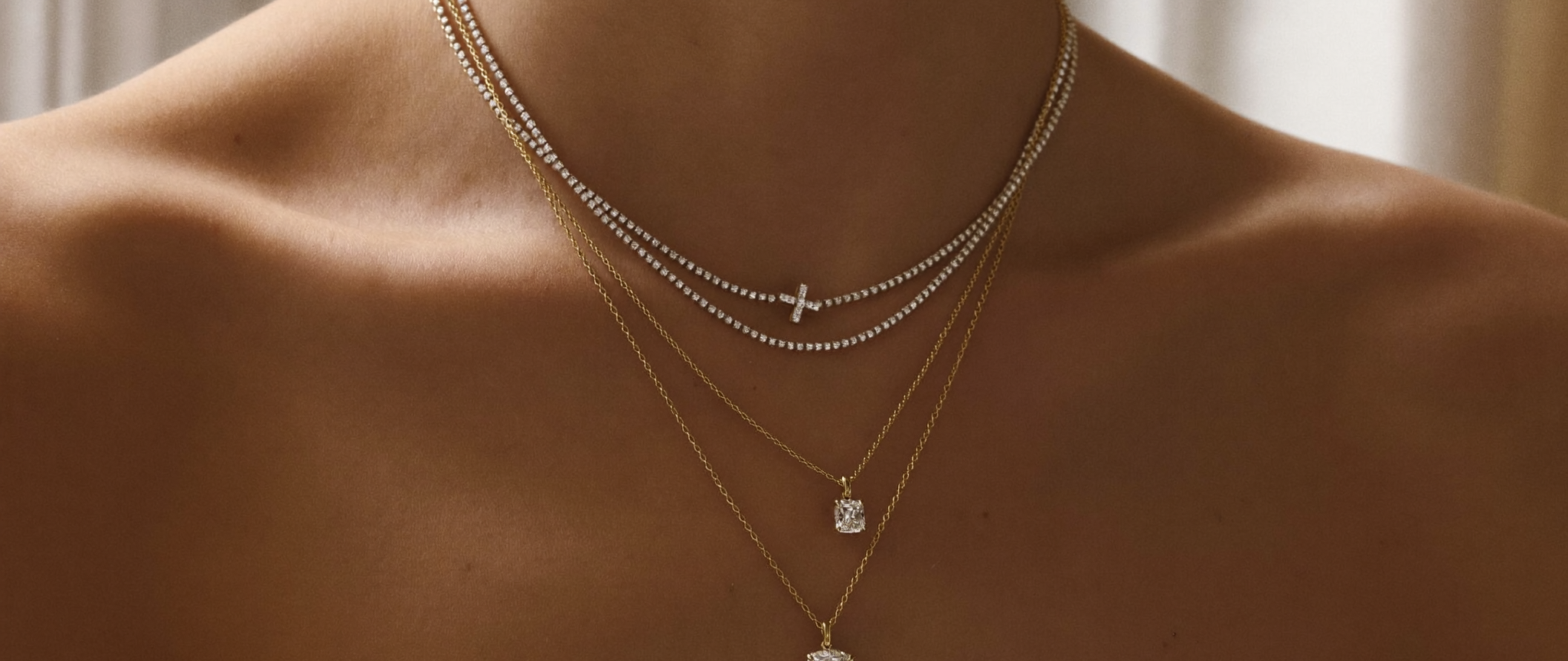 Layered diamond necklaces at varying lengths in solid gold on a neckline, showing how to layer necklaces, in natural light