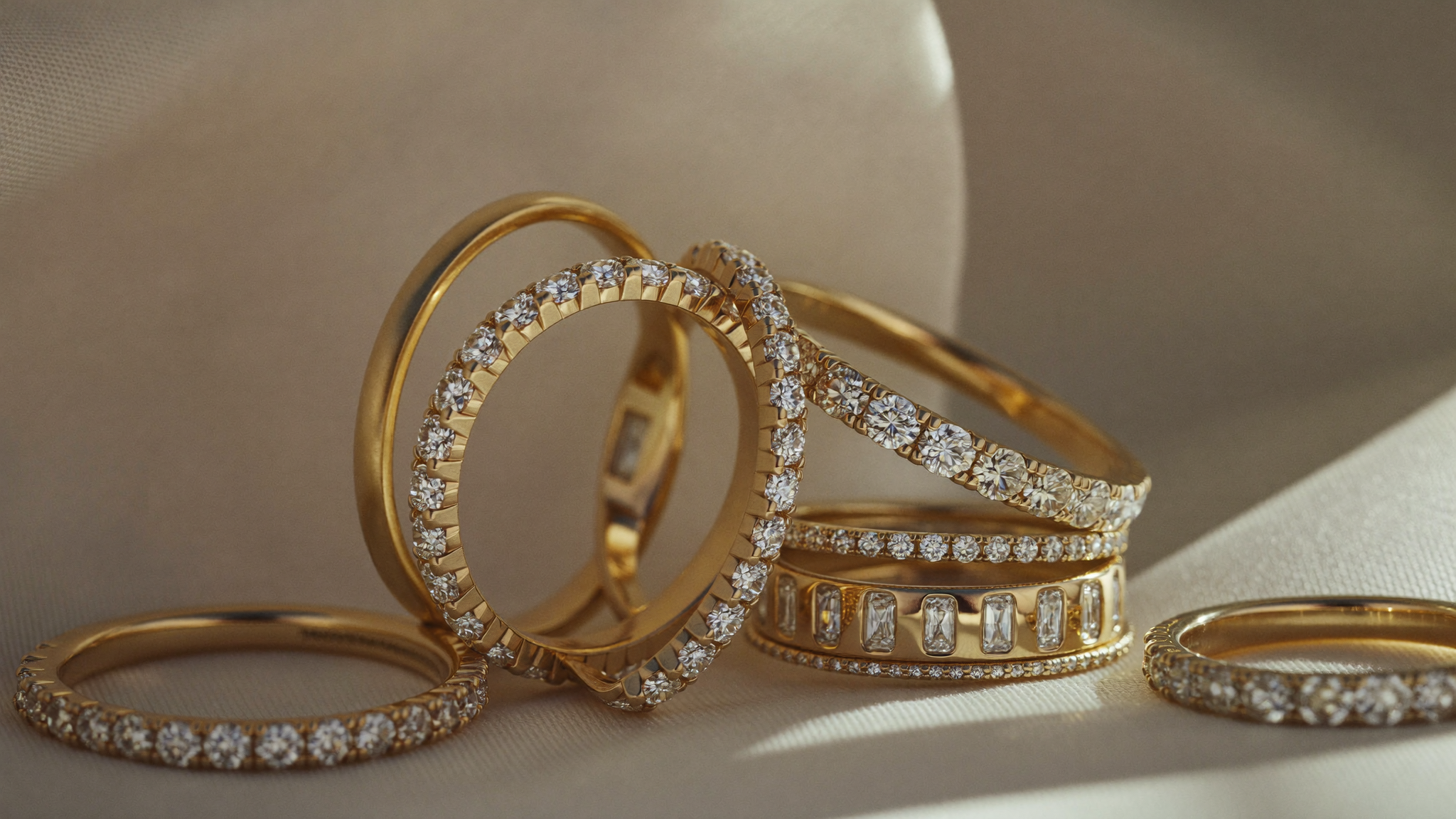 Stack of solid gold diamond bands in 10k, 14k and 18k yellow gold on ivory silk in natural light