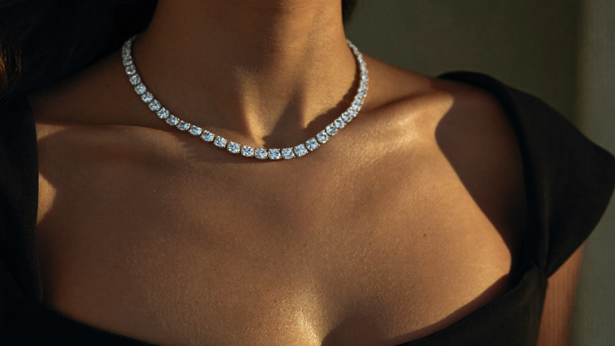 Close-up of a woman wearing a diamond tennis necklace, a riviere line of lab-grown diamonds, in warm evening light