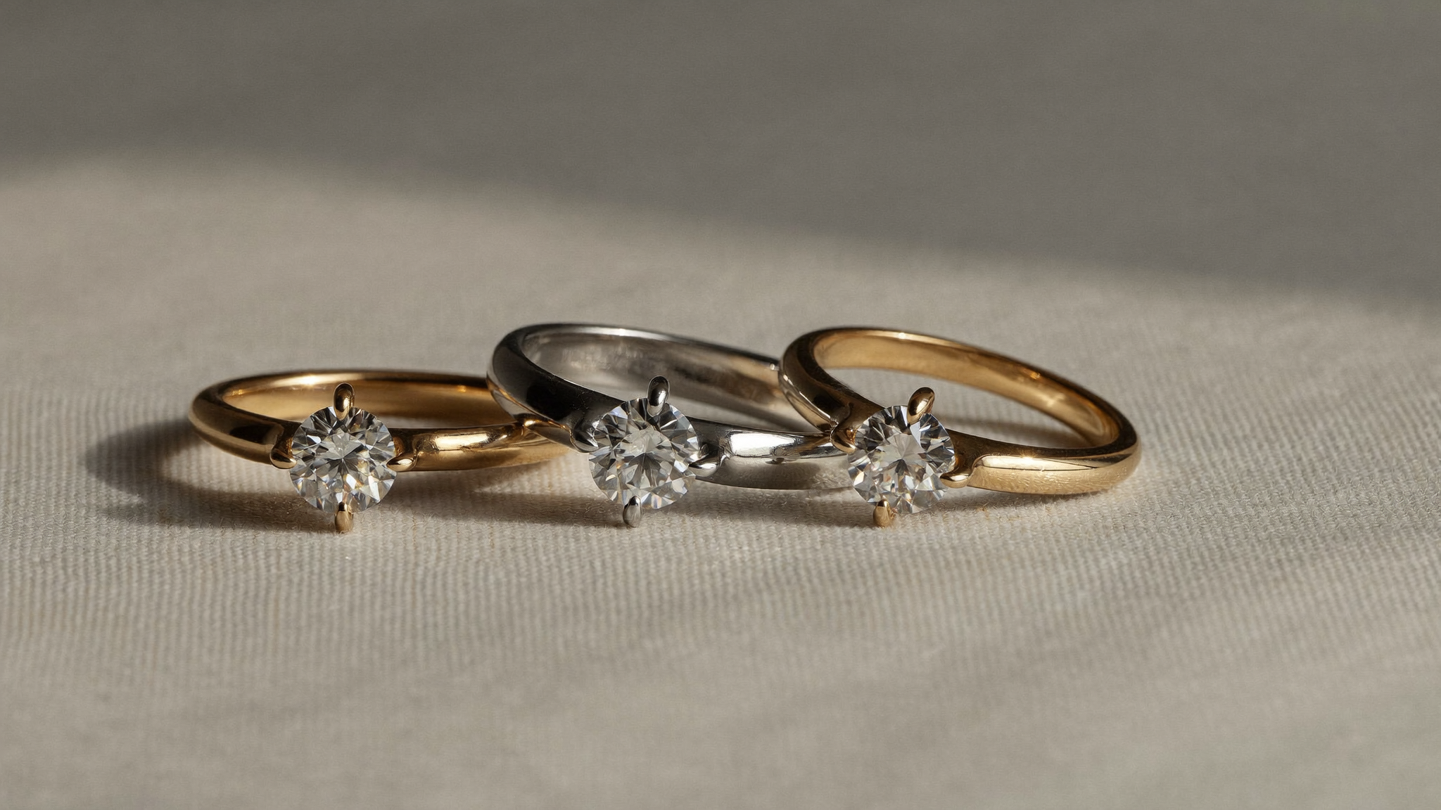 Yellow gold, white gold, and rose gold diamond rings side by side on linen in natural light