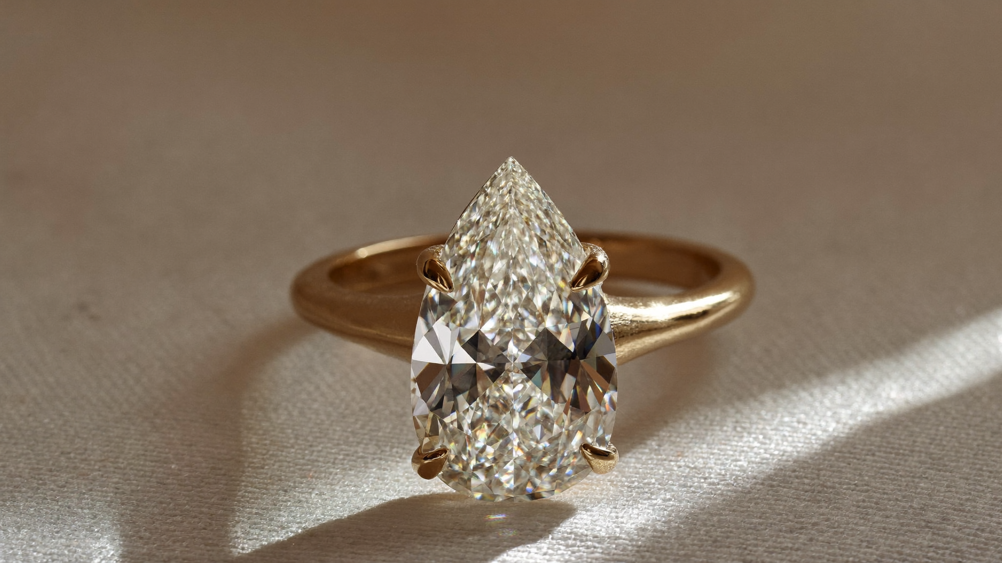 Pear cut diamond solitaire ring in solid gold resting on ivory linen in soft natural light