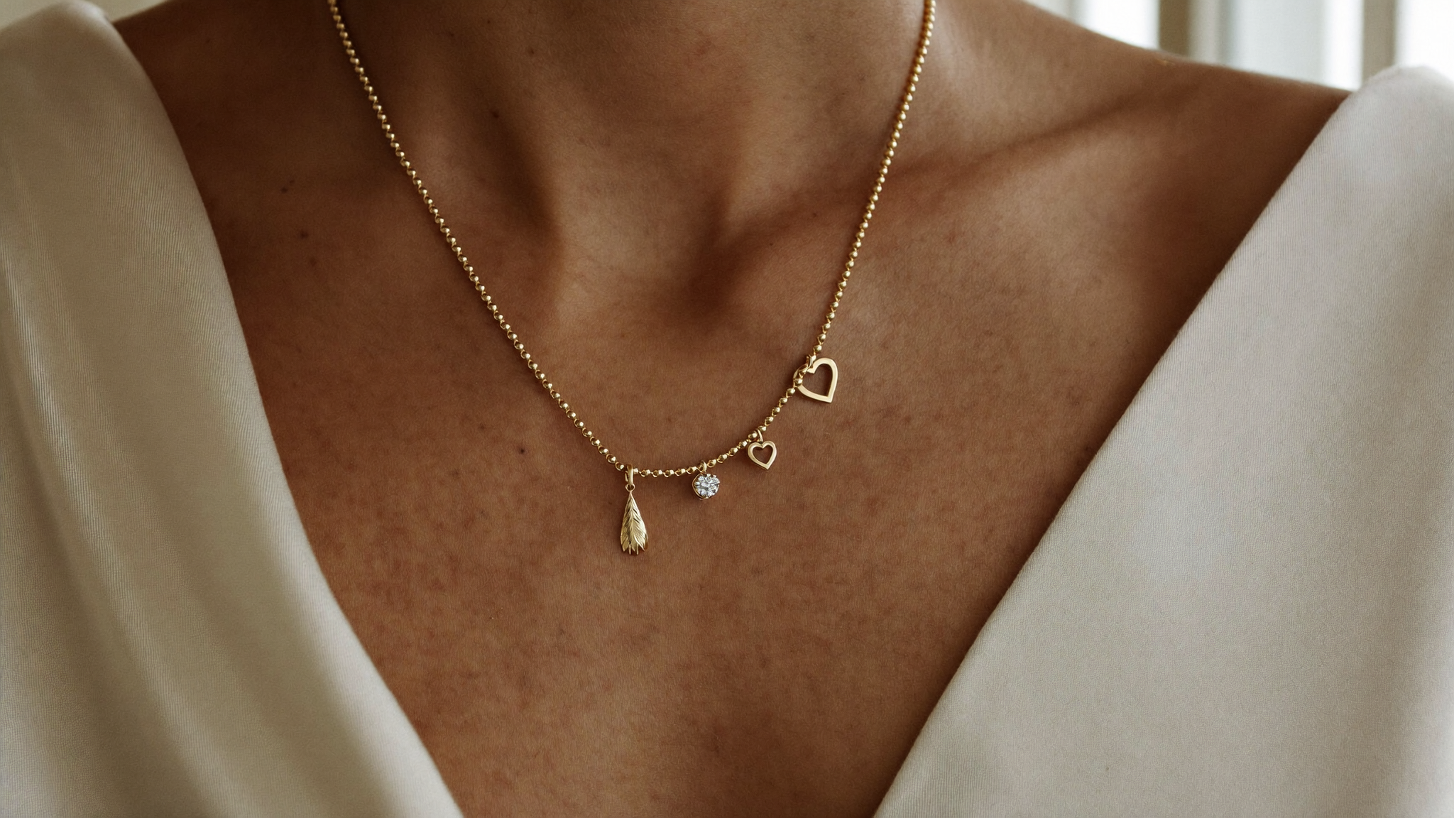 Gold charm necklace layered with diamond heart and marquise charms resting on the collarbone