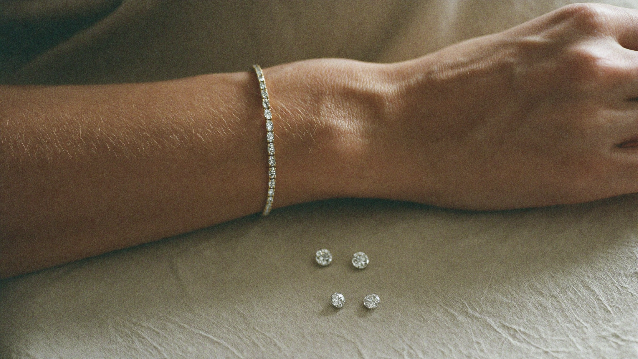 Lab grown diamond tennis bracelet on a woman's wrist beside loose round diamonds on cream linen in natural light