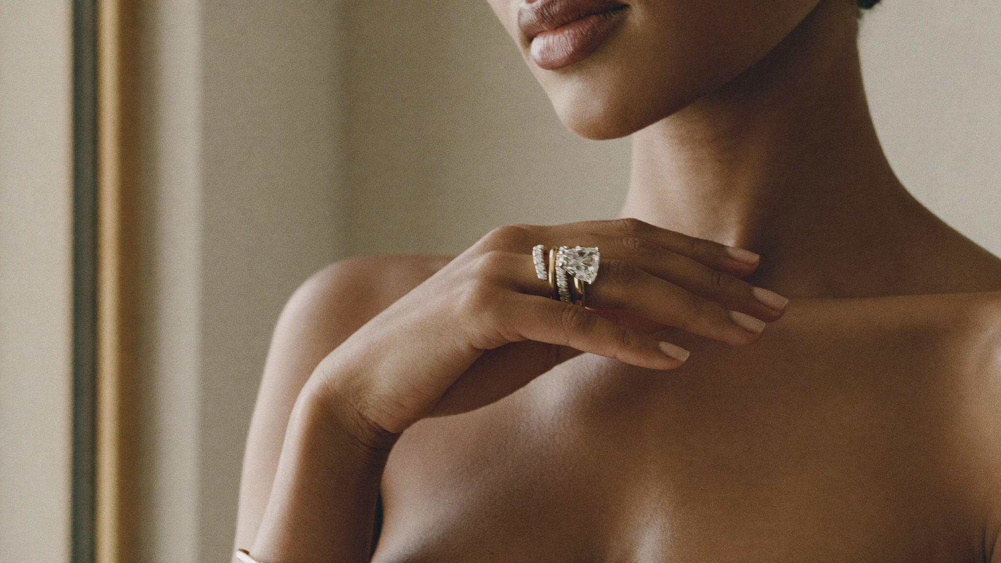 A woman's right hand raised at her collarbone wearing a bold lab grown diamond right-hand ring and stacked gold band