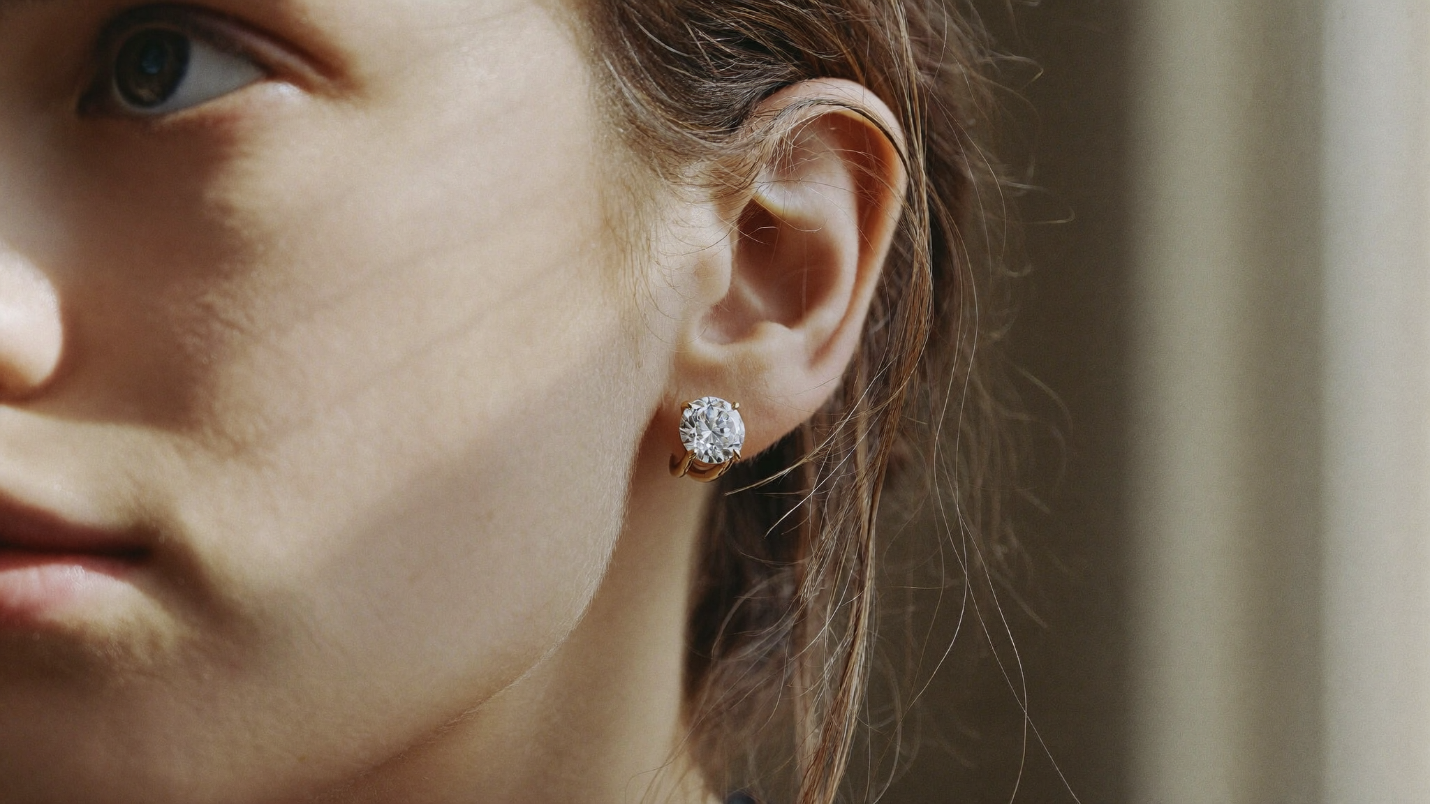 Close-up of a round lab-grown diamond stud earring in yellow gold on a woman's ear in natural light