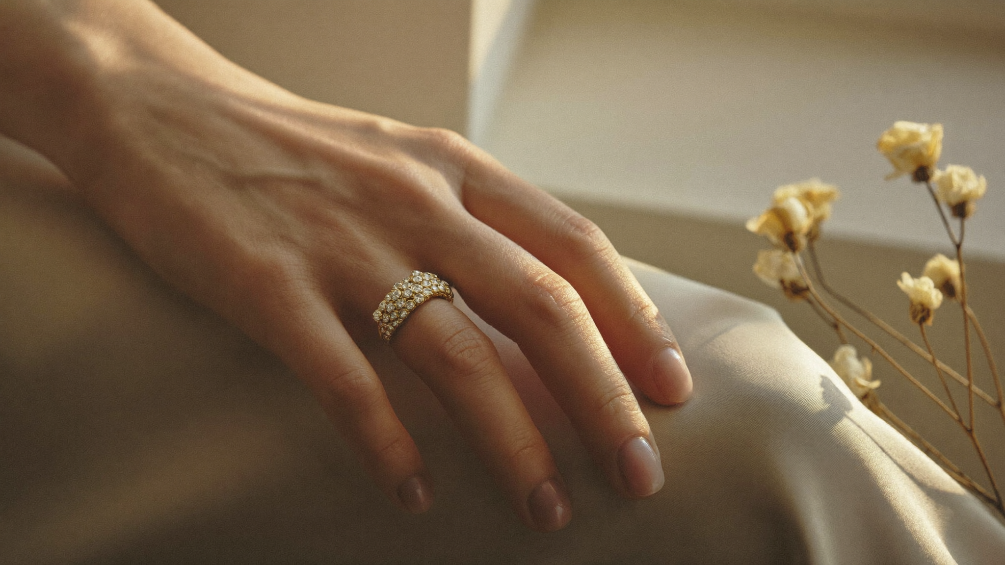 Close-up of a diamond eternity band in solid yellow gold on a hand in warm golden light