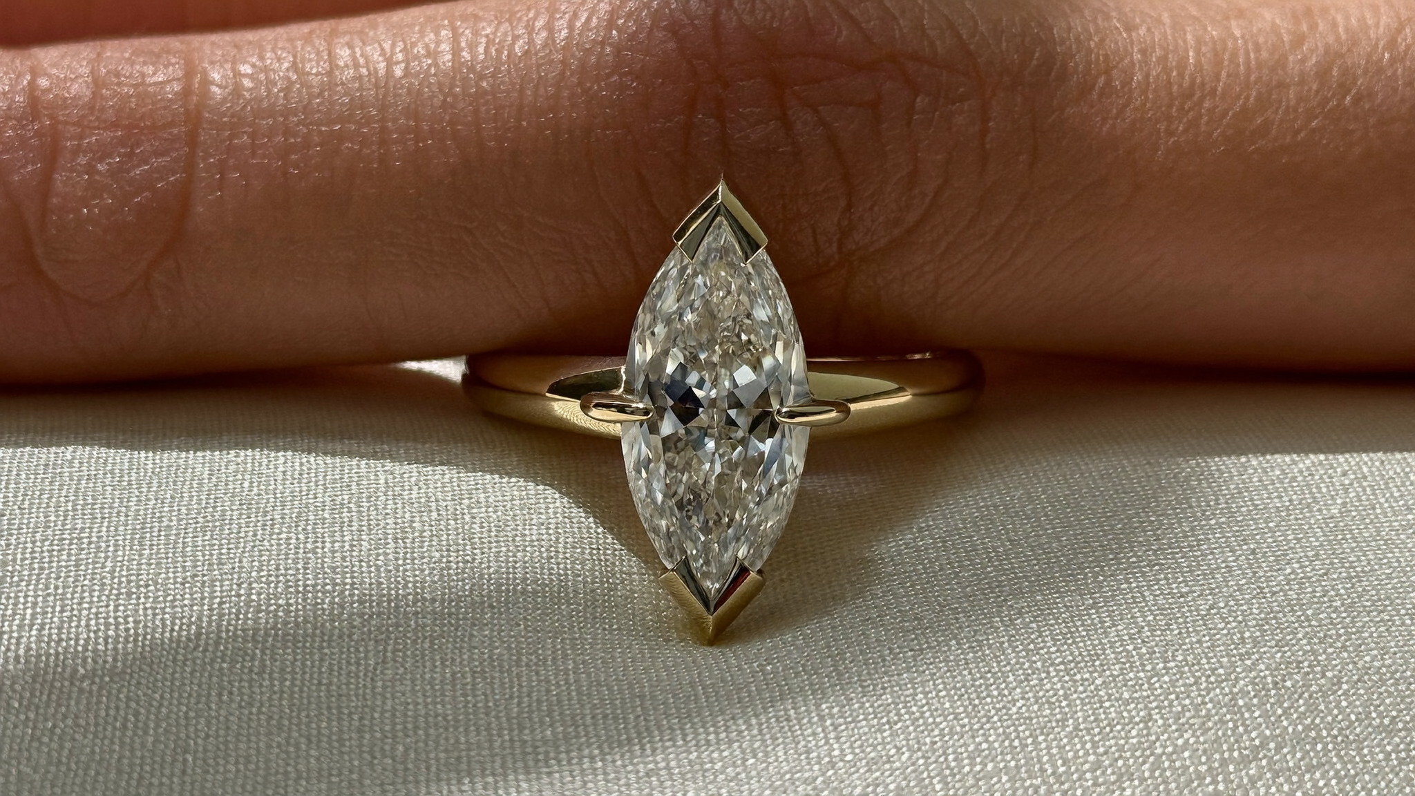 Close-up of a marquise cut diamond ring in yellow gold resting on ivory silk in soft natural light
