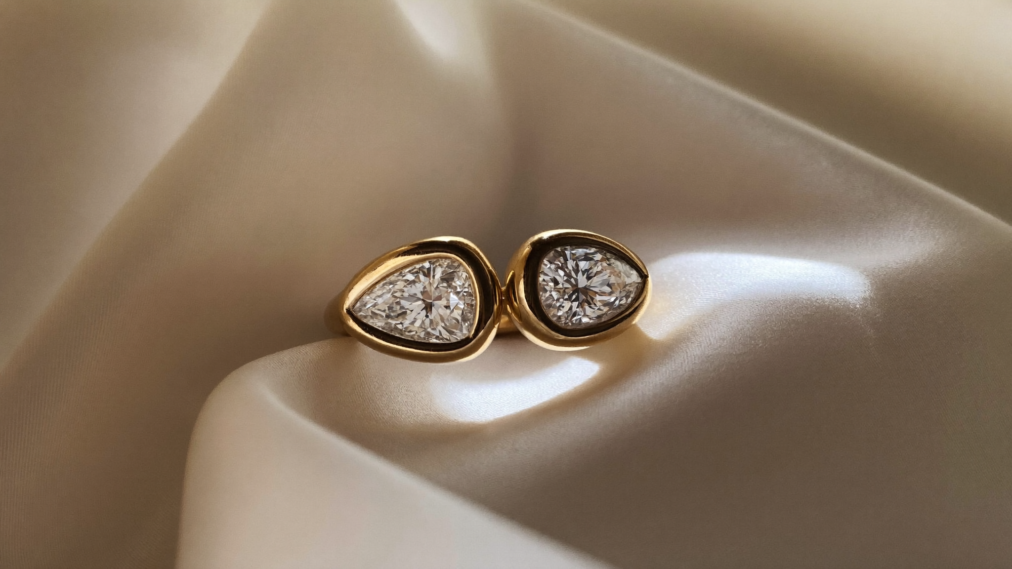 Two pear-cut lab-grown diamonds set side by side in a gold toi et moi ring on ivory silk