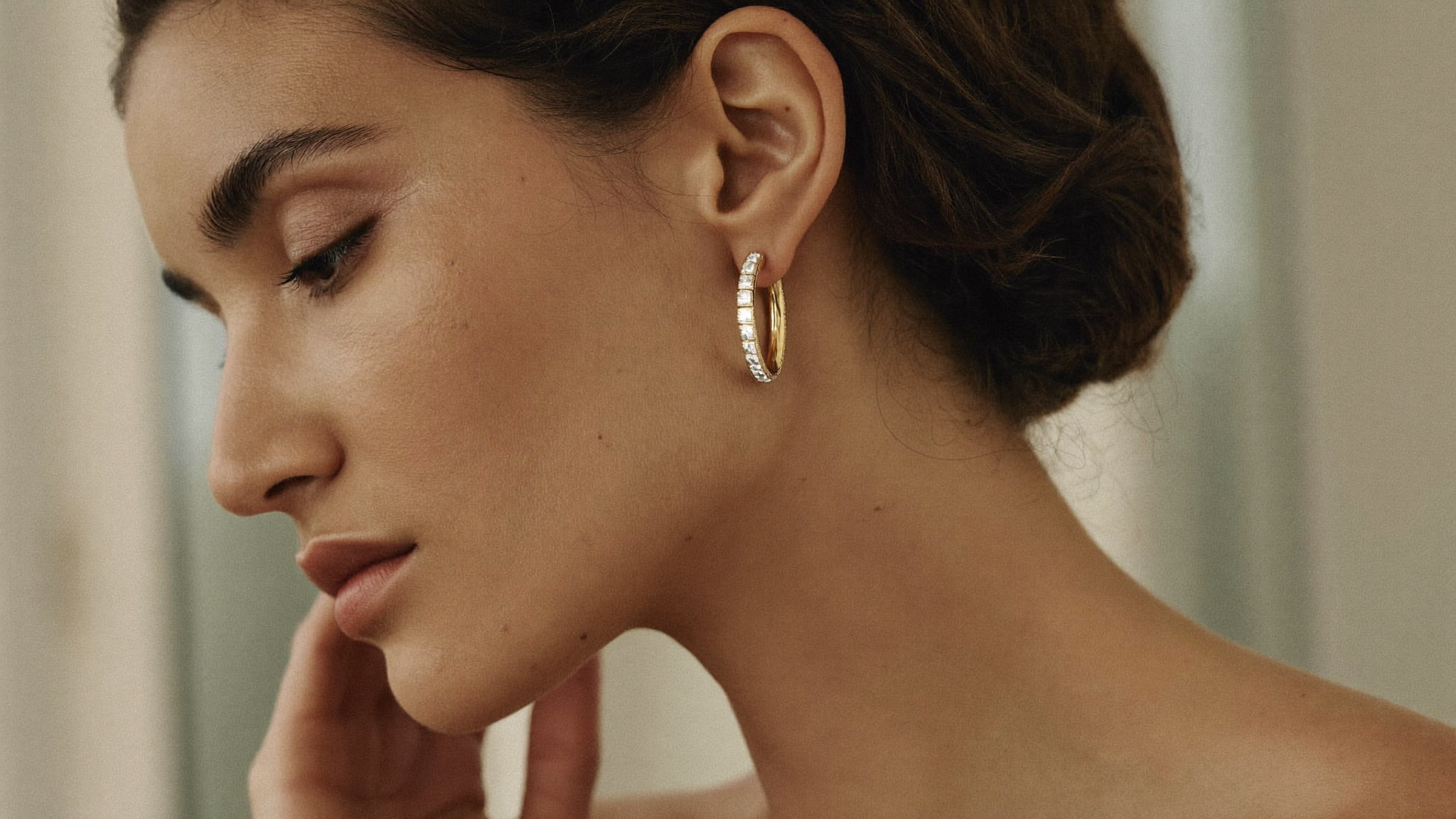 Close-up side profile of a woman wearing a slim gold diamond hoop earring in soft natural light