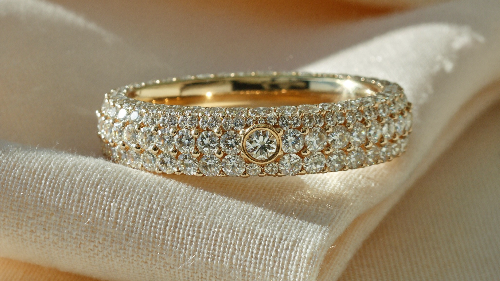 Close-up of a pavé setting gold diamond ring paved with tiny diamonds on cream linen in natural light
