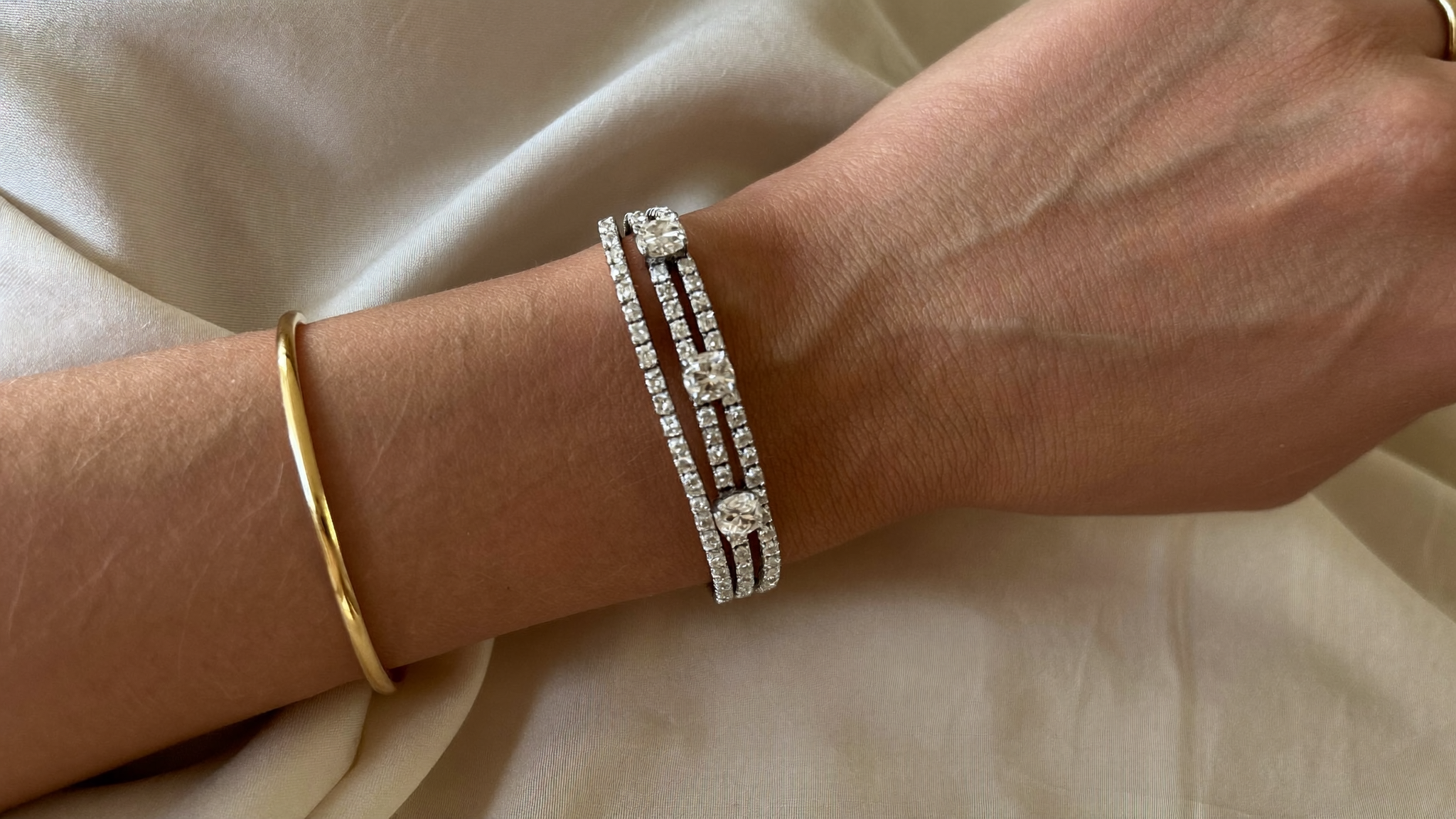 How to stack bracelets: lab grown diamond tennis bracelets layered with a gold bangle on a wrist in warm light