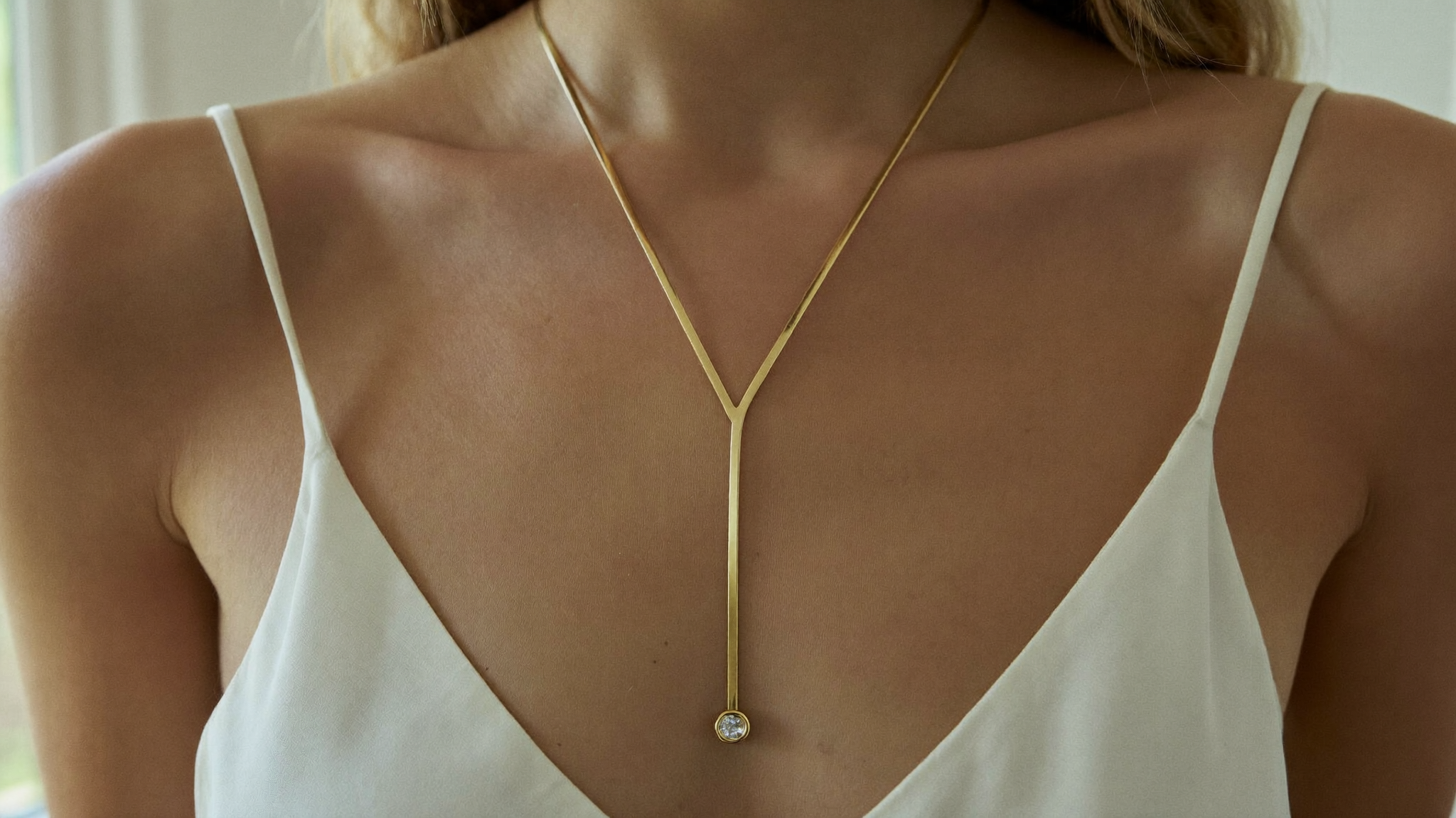 Woman wearing a long gold lariat necklace with a diamond drop pendant in a Y-line on bare decolletage, natural light