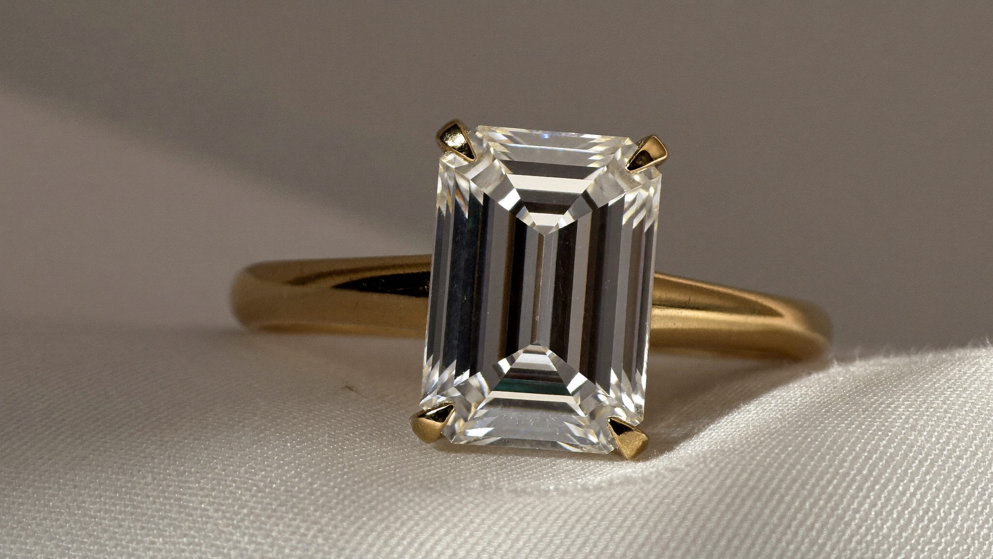 Close-up of an emerald cut diamond ring in solid gold on ivory linen, natural light