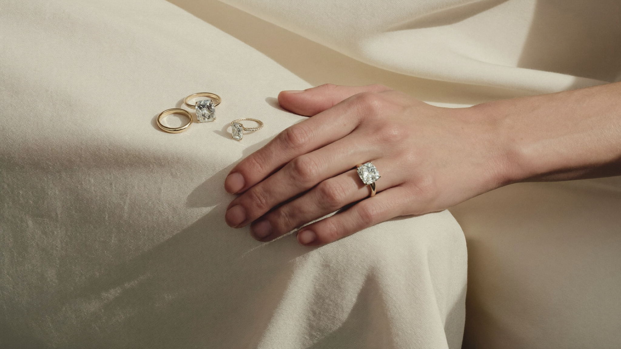 Diamond carat size guide: a hand wearing a solitaire lab-grown gold diamond ring beside rings of different carat sizes on cream linen