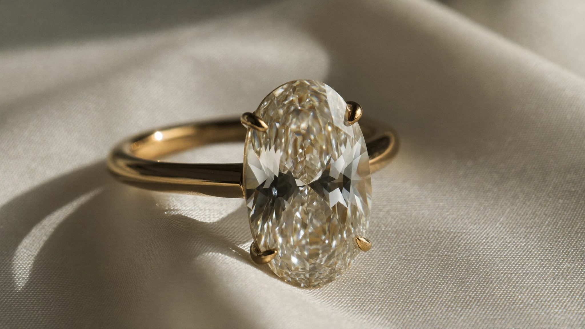 Oval cut diamond solitaire ring in yellow gold resting on ivory silk in soft natural light