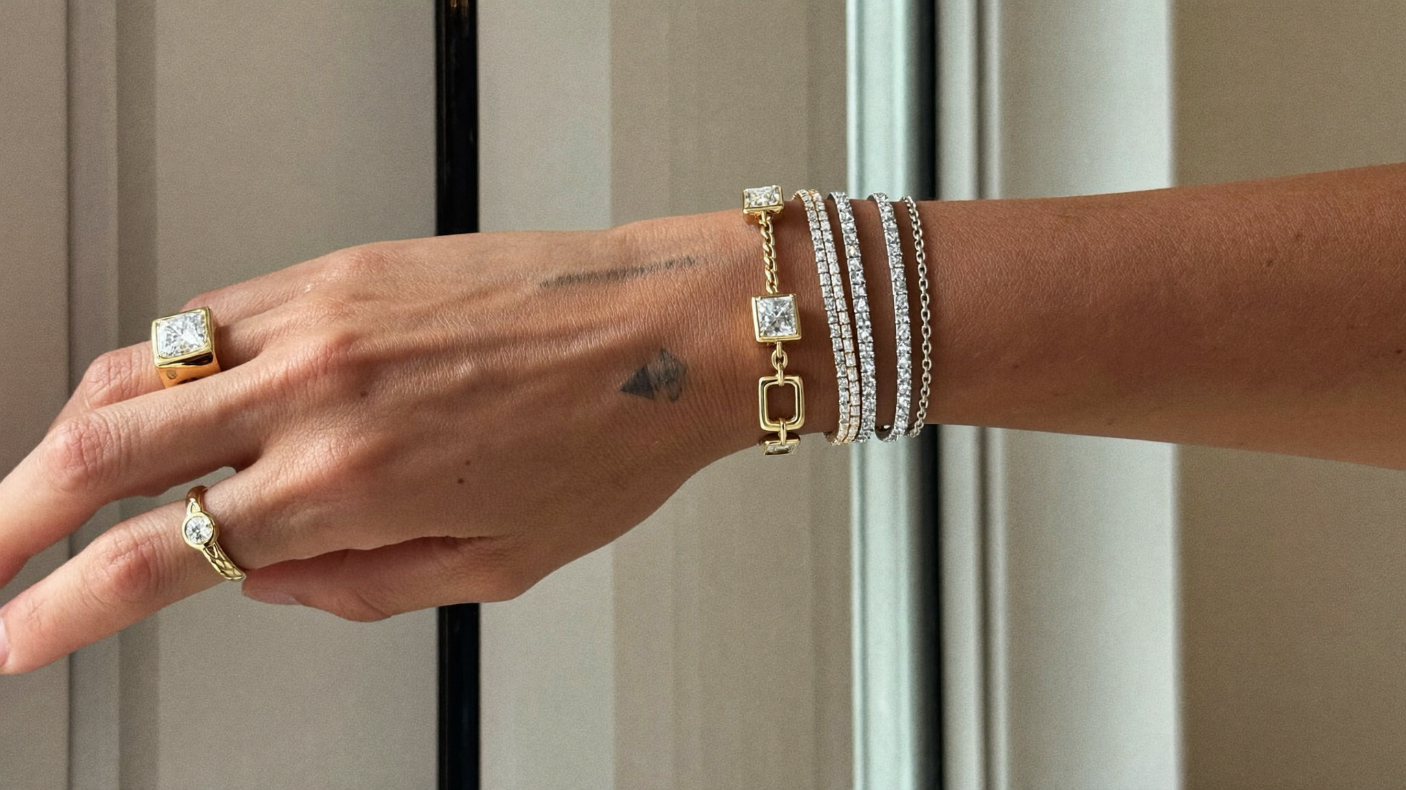 Mixed metal jewelry stacked on a wrist, yellow gold and white gold diamond bracelets and rings in soft natural light