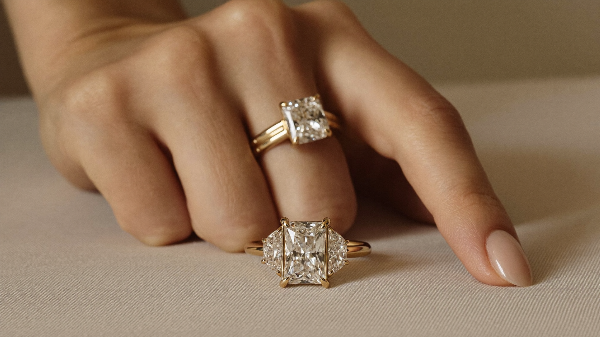 Close-up of a yellow gold three-stone engagement ring with three round lab grown diamonds on warm linen