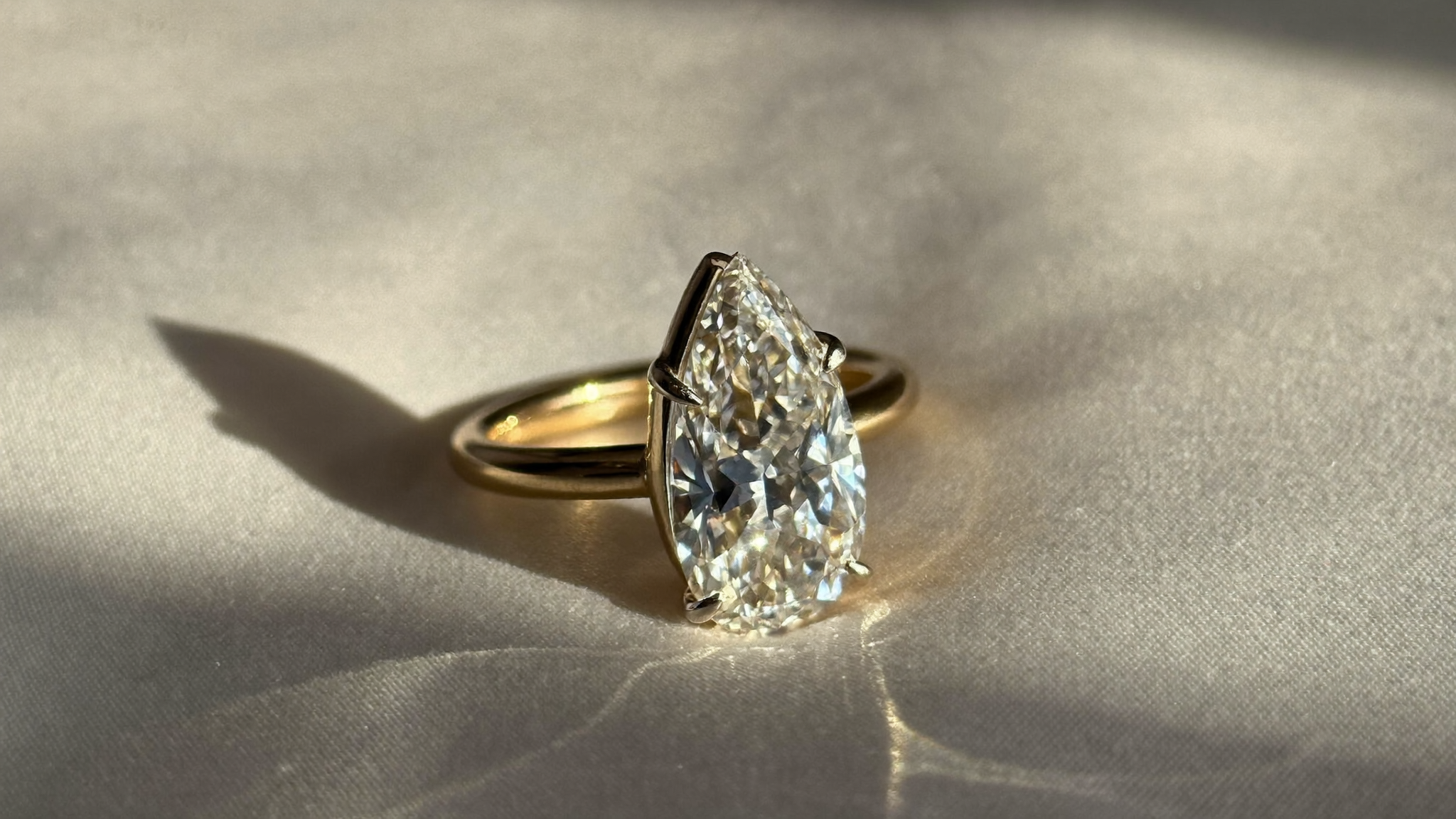 Pear cut diamond solitaire ring in yellow gold resting on ivory silk in warm natural light