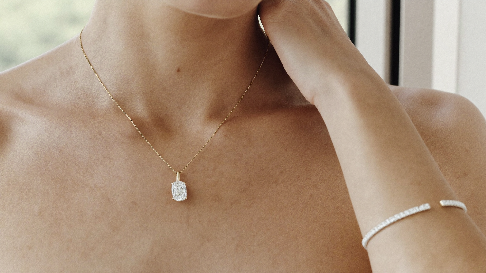 Quiet luxury jewelry on a neckline, a delicate diamond solitaire pendant and slim gold tennis bracelet in soft natural light