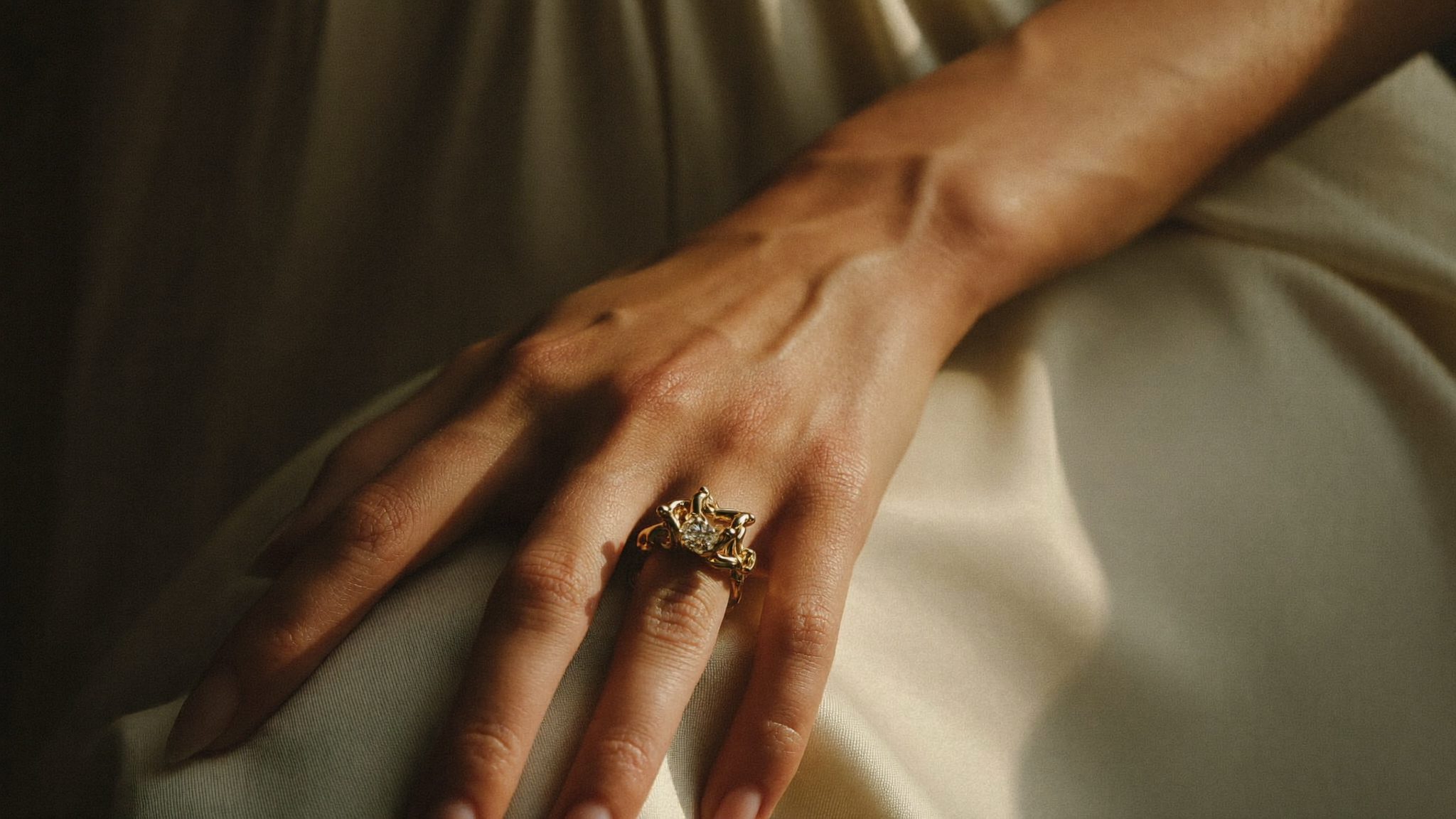 Custom engagement ring ideas, a sculptural gold lab grown diamond ring on a hand resting on cream silk