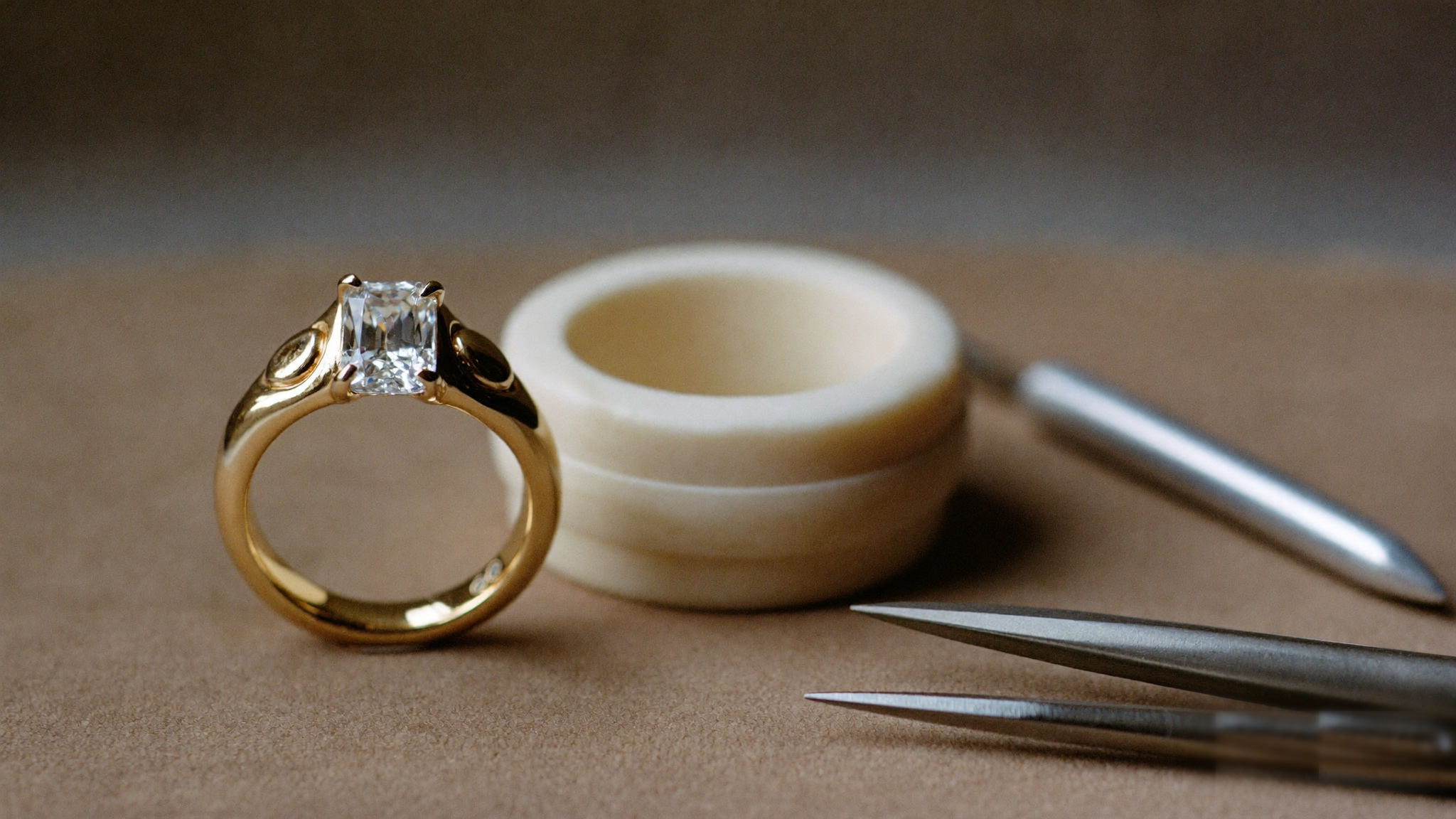 How custom engagement rings are made, a solid gold lab grown diamond ring beside a carved wax model and jeweler tools
